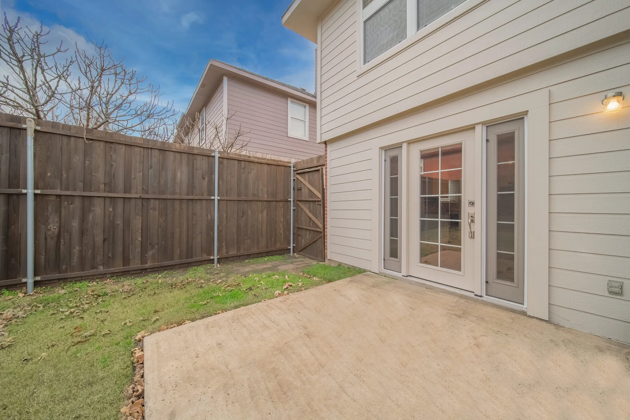 Private outdoor patio with a wooden fence, accompanied by a glass-paned door and sidelights