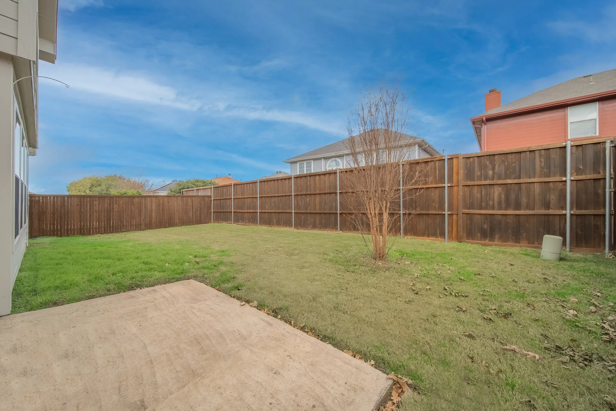Expansive backyard featuring a concrete patio, wood privacy fencing, and a mature tree