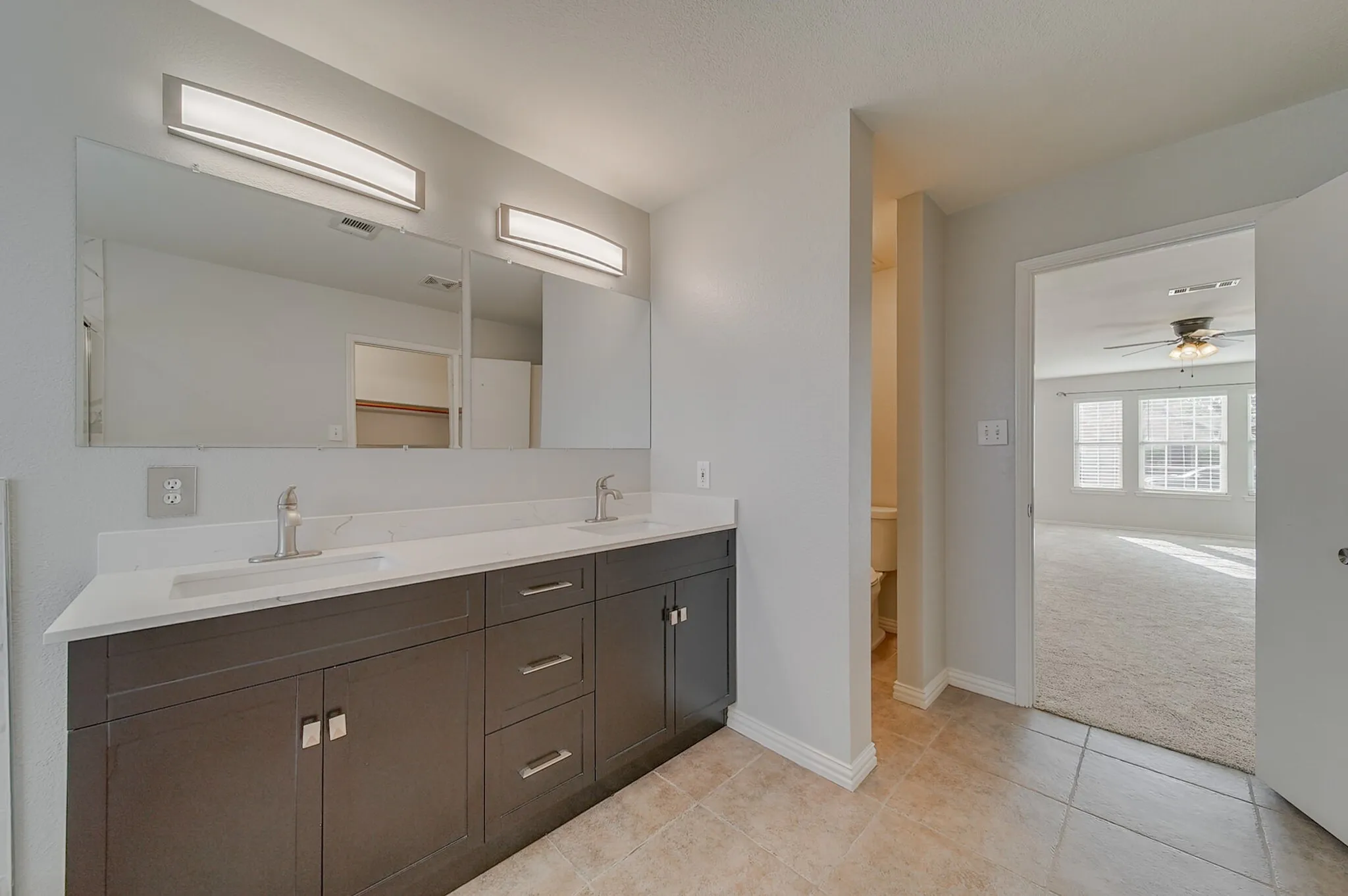Dual vanity with a white countertop and rectangular sinks, framed by a large mirror and two overhead light fixtures