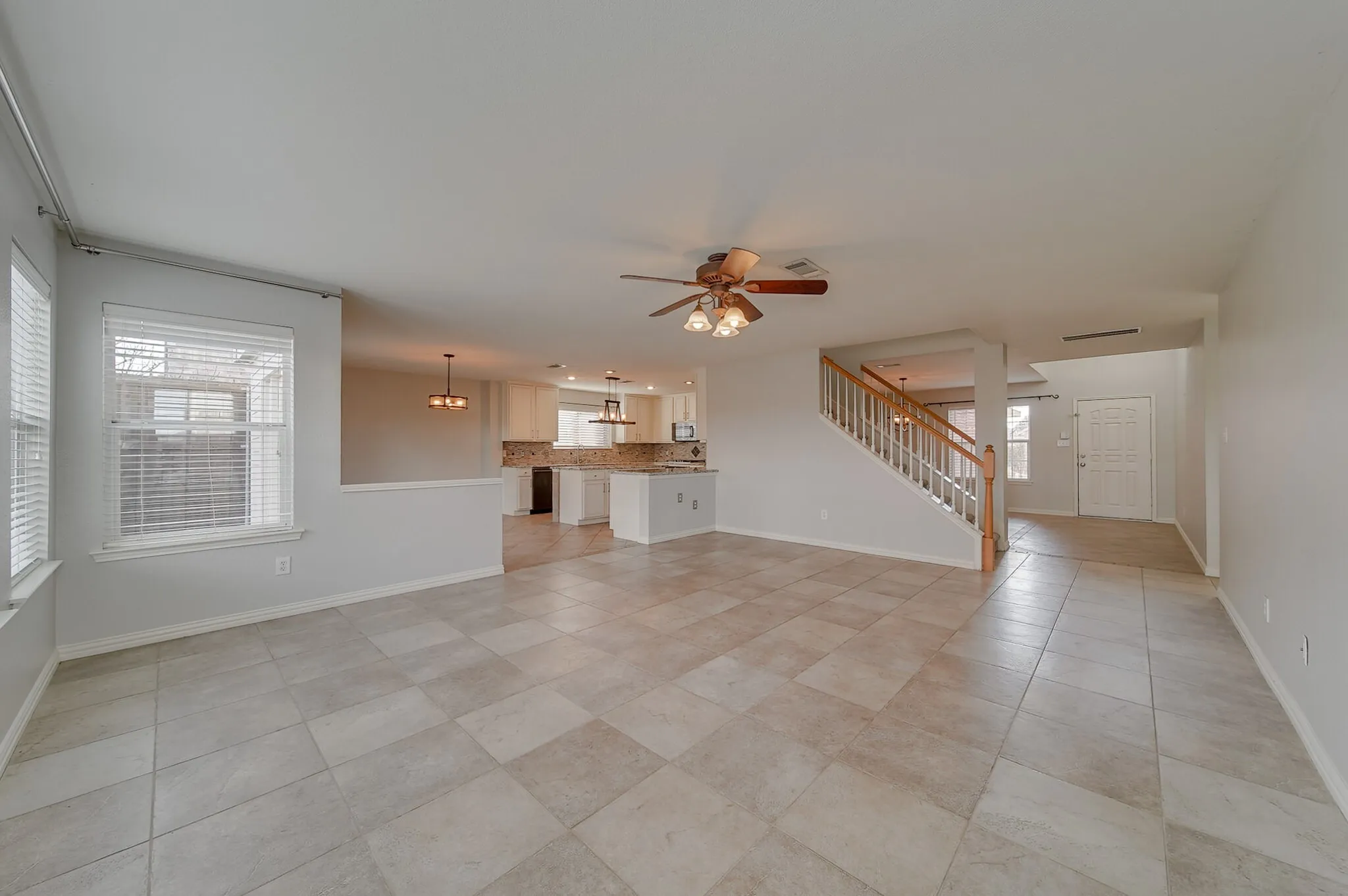 Tile flooring throughout, staircase with wood handrails and white balusters, and a ceiling fan with light fixture