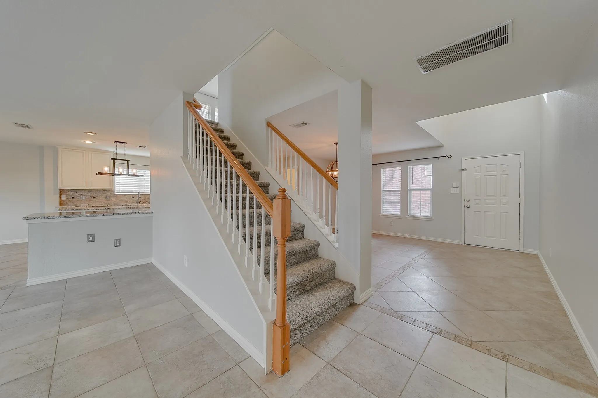 Carpeted staircase with wood handrails, tile flooring, kitchen with white cabinetry and stone countertops, and an entry door with panel detailing