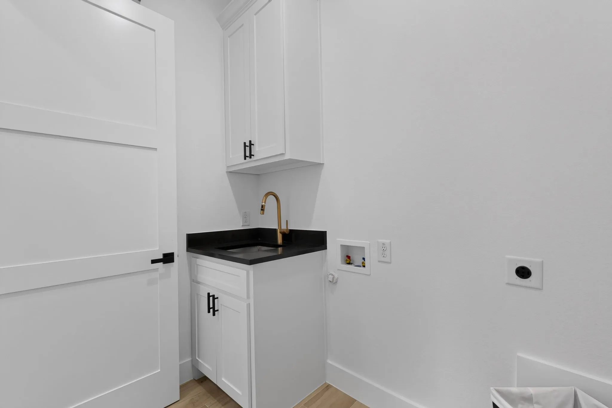 White cabinetry with black hardware, dark countertop, gold-finish faucet, and light wood-finish flooring