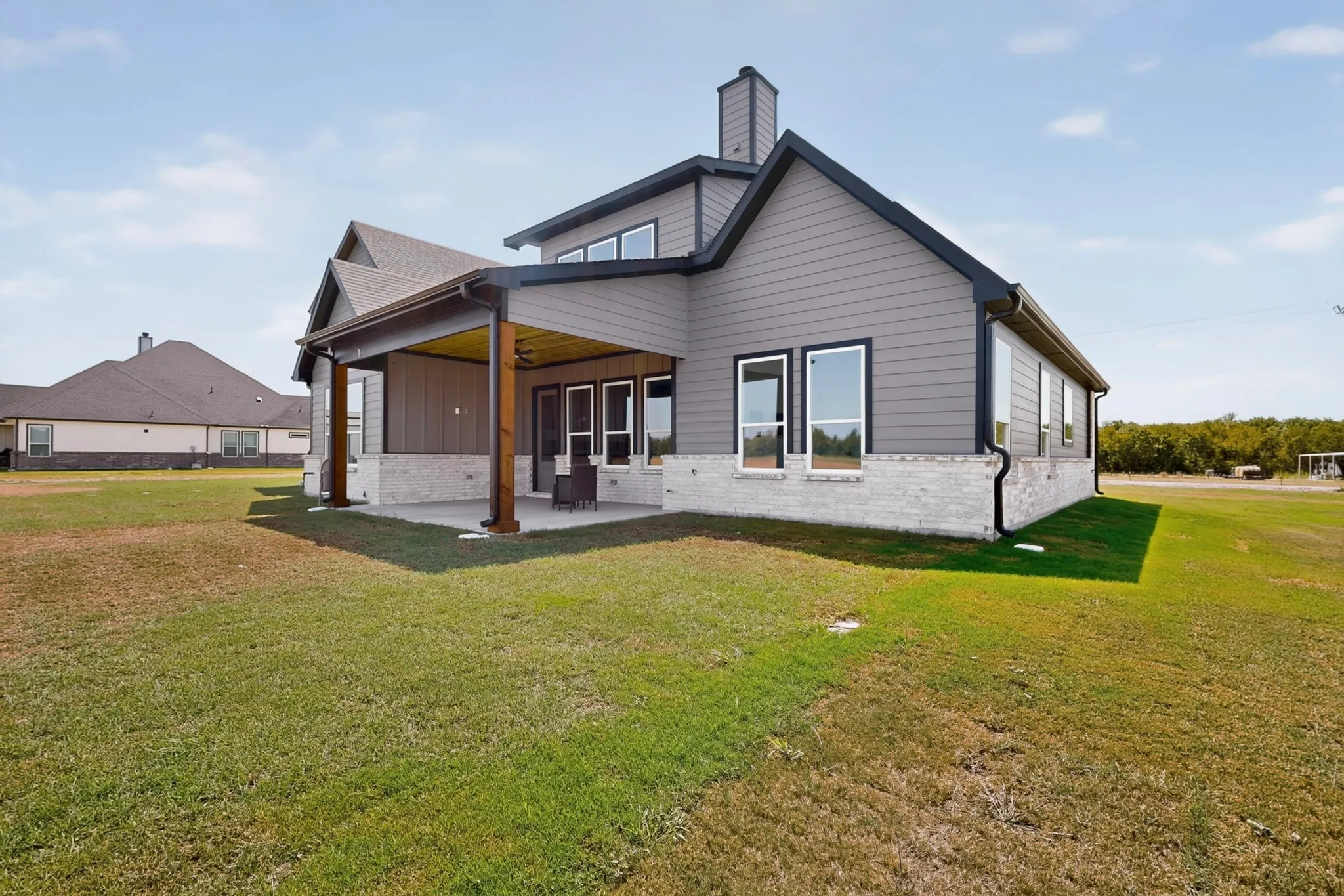 Expansive backyard with a covered patio featuring a built-in ceiling fan, wood-toned support beams, and gray siding with a white brick facade