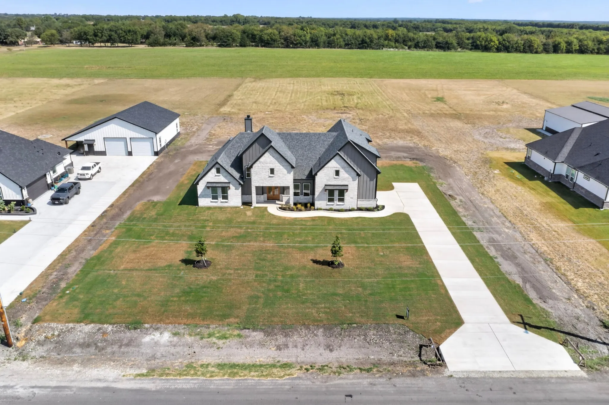 Modern farmhouse-style exterior with stone and siding accents, dark gabled roofing, a covered entry, and a concrete driveway