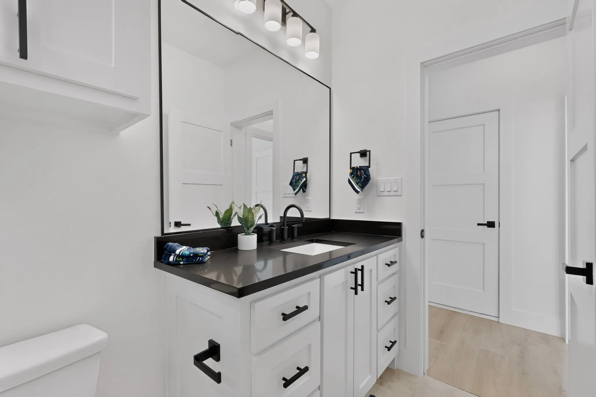 White shaker vanity with black hardware, dark countertop with integrated sink, black wall-mounted faucet, and a large mirror with a black frame