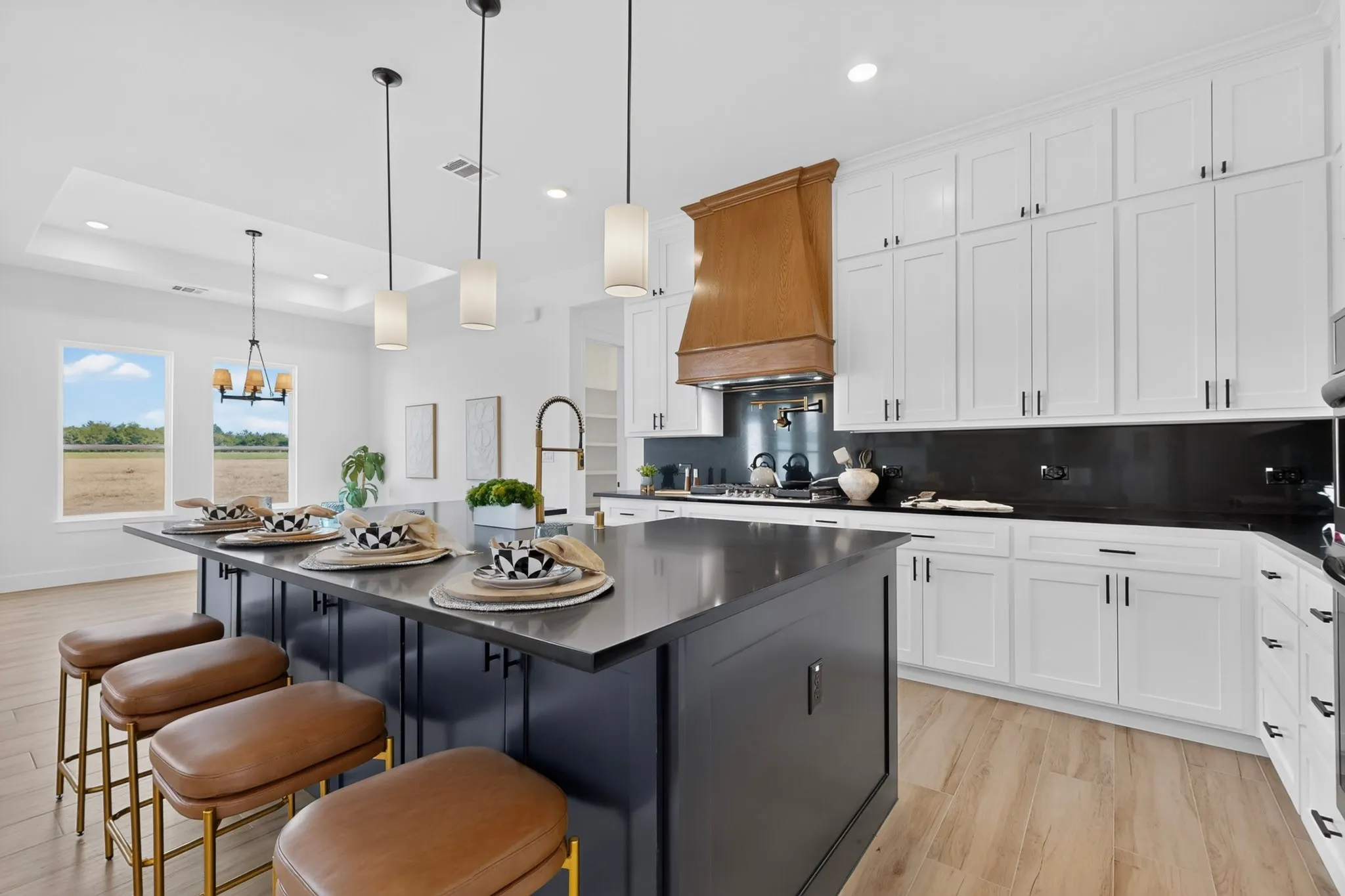 Spacious kitchen featuring an expansive center island, white shaker cabinetry, a wood-finish range hood, dark countertops, and light wood-finish flooring