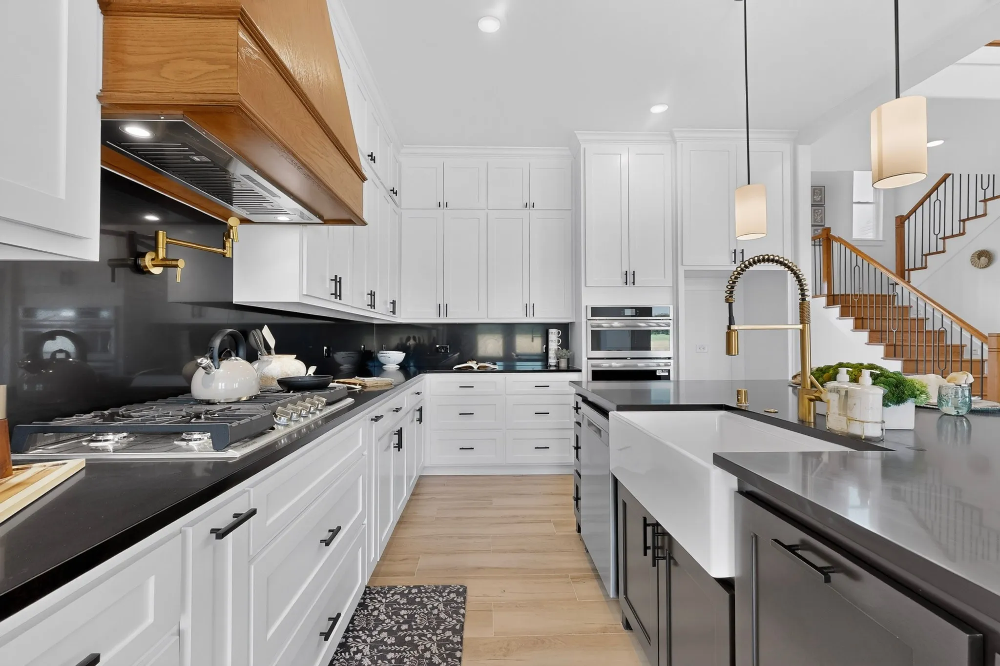 Gourmet kitchen with white shaker cabinetry, dark countertops, a large center island with a farmhouse sink, and a wood-finish range hood
