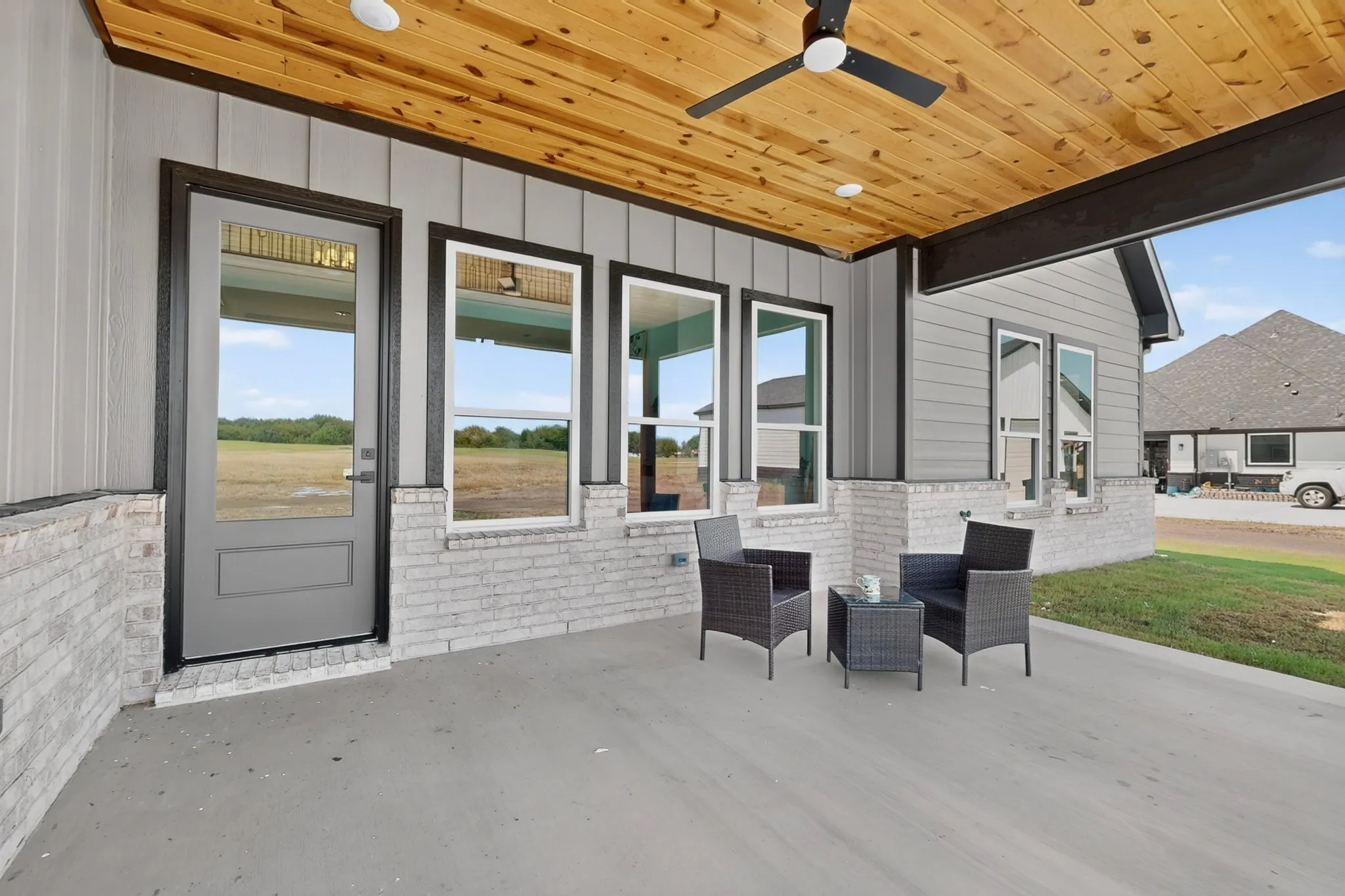 Covered patio featuring a wood-finish ceiling, ceiling fan, and white brick accents