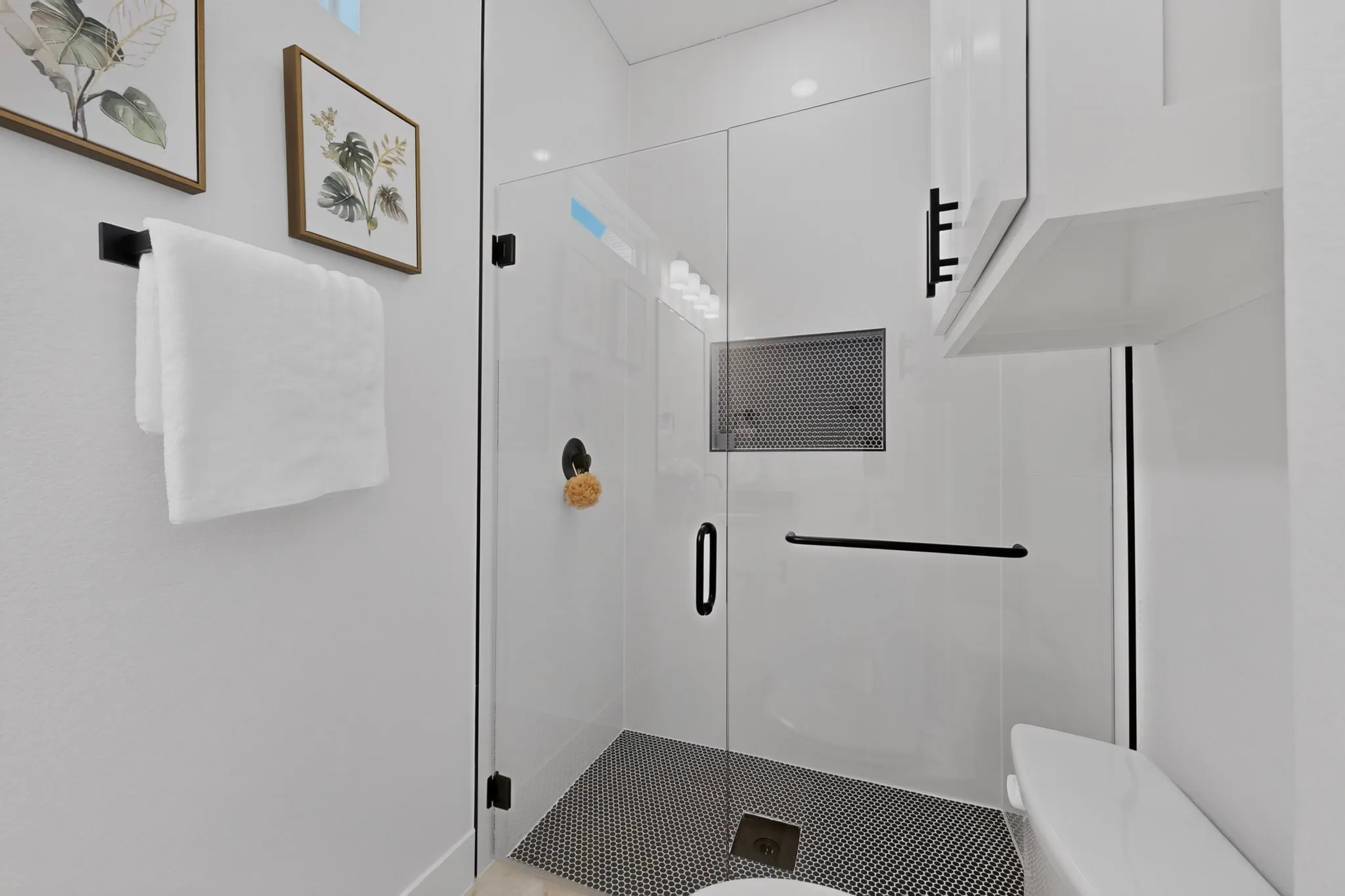 Glass-enclosed shower with black penny tile flooring and built-in shower niche