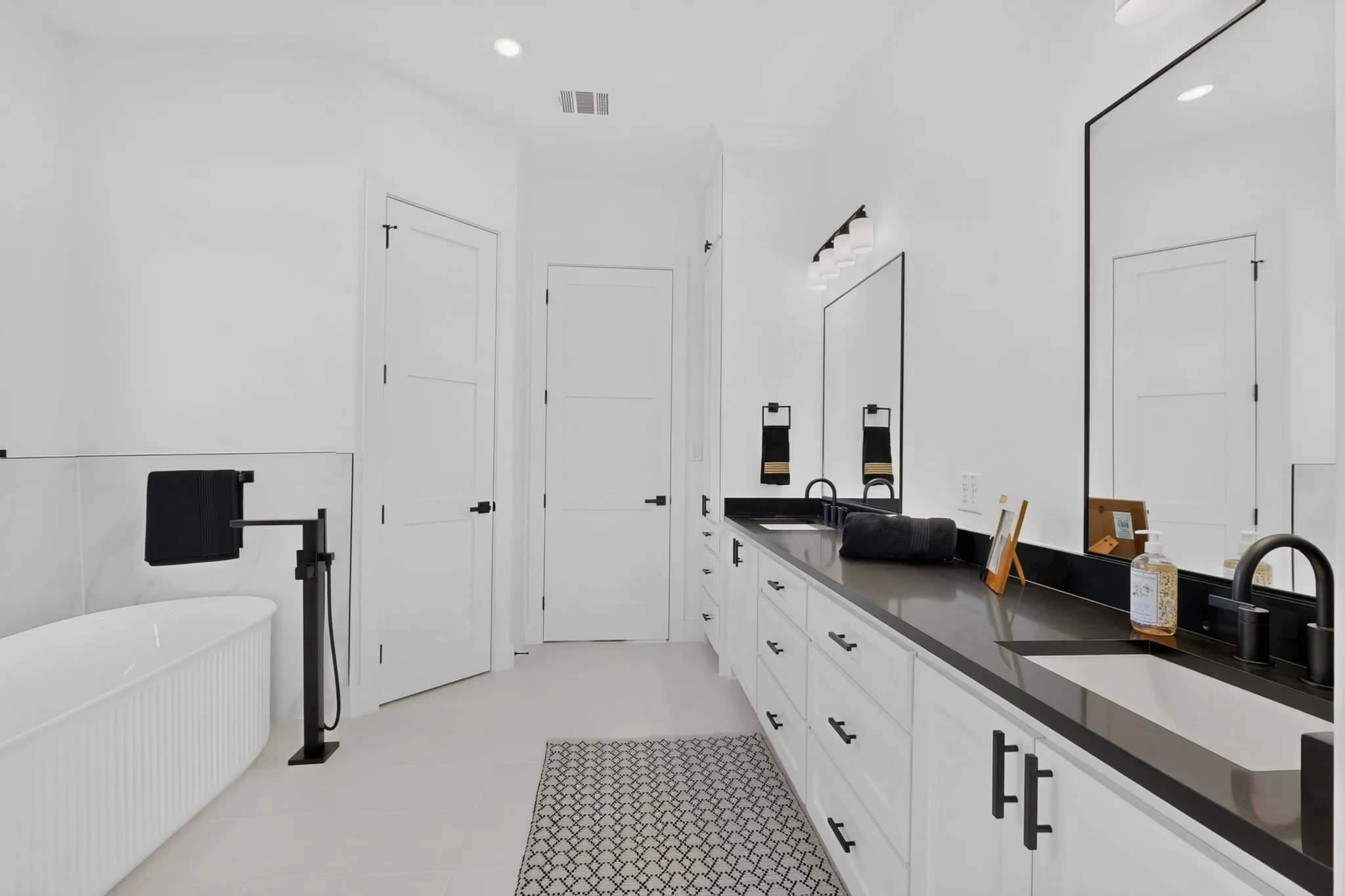 Freestanding soaking tub with floor-mounted fixture, dual vanity with undermount sinks, dark countertops, and large framed mirrors