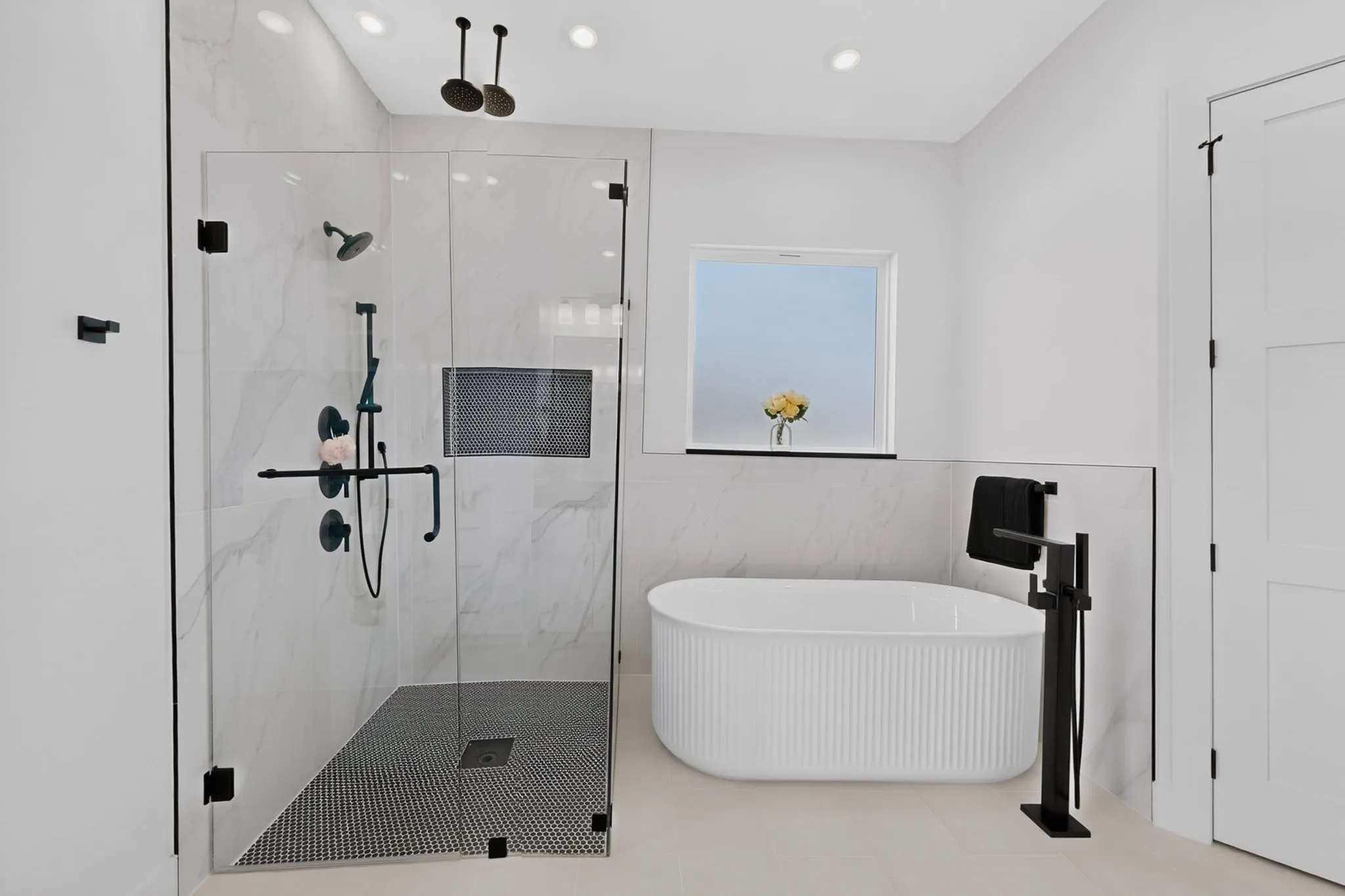 Glass-enclosed shower with black penny tile flooring, a built-in niche, and a contrasting free-standing soaking tub with a floor-mounted fixture