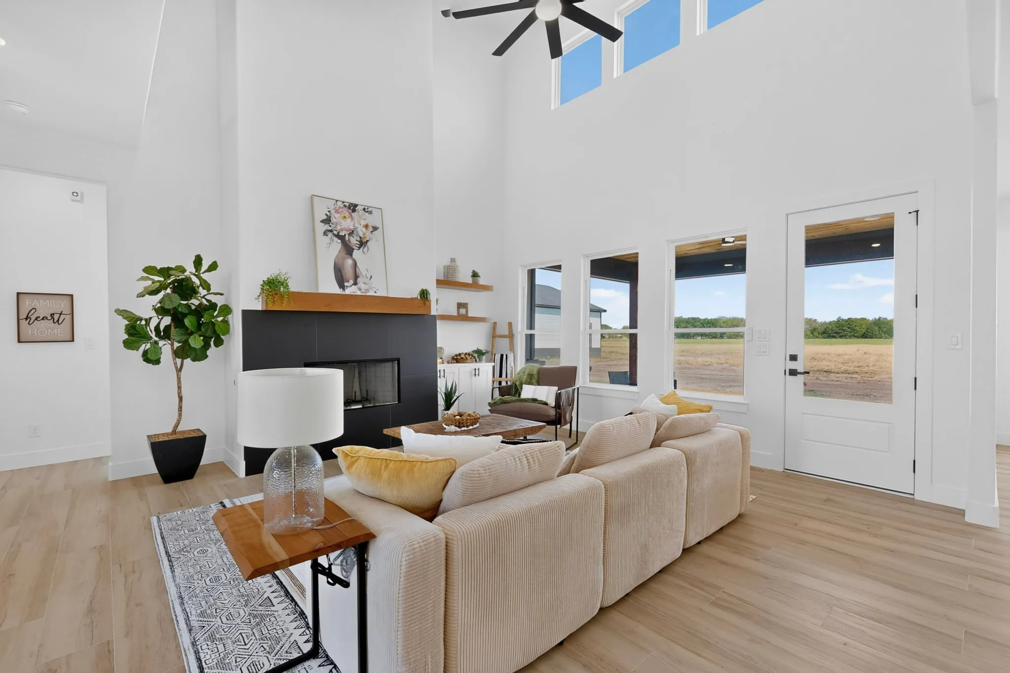 Vaulted ceiling with a ceiling fan, a black fireplace with a wood mantel, wood-finish flooring, and multiple large windows