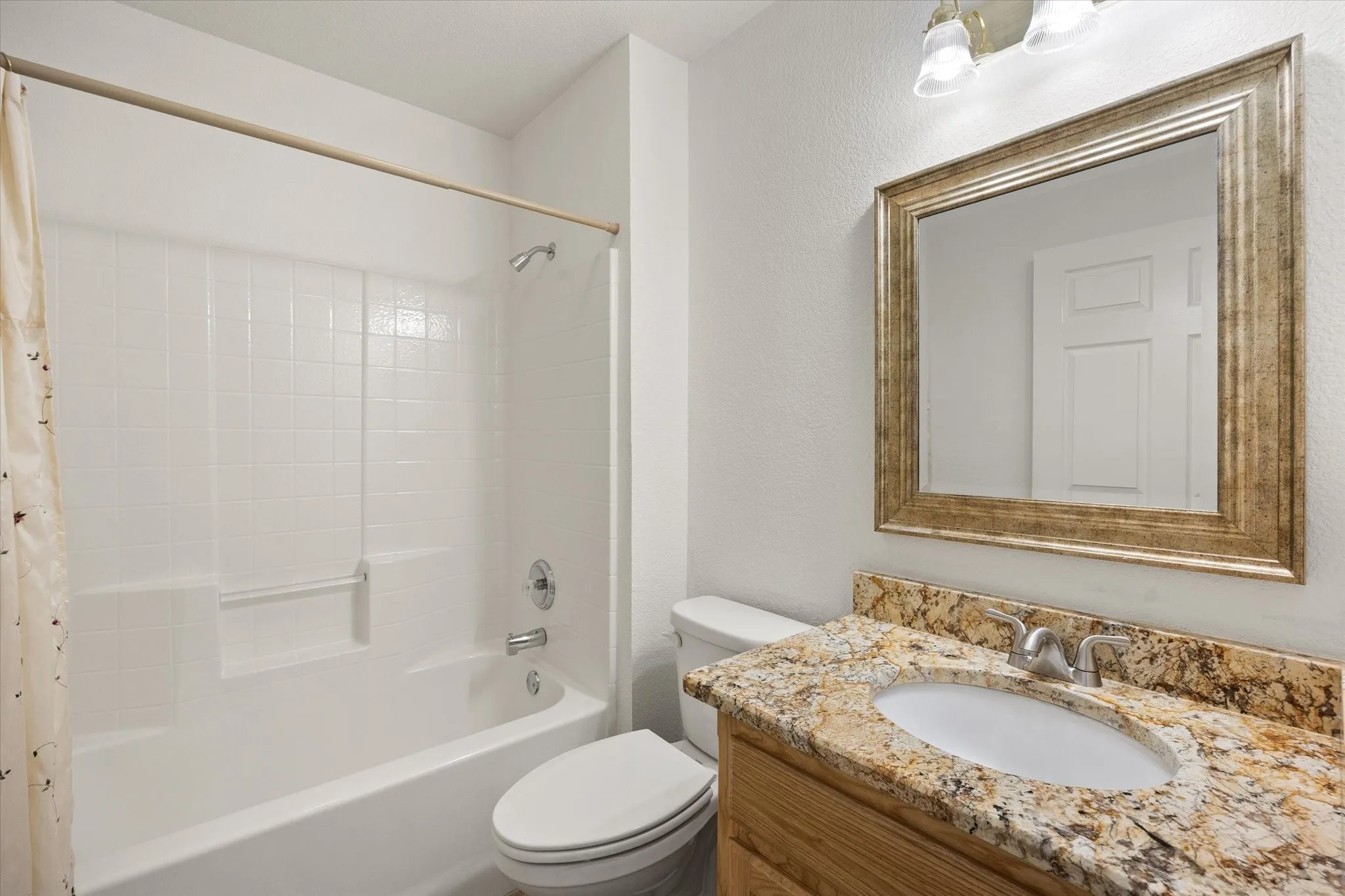 Guest bathroom granite vanity with an undermount sink, a framed mirror, and a full bathtub/shower combo