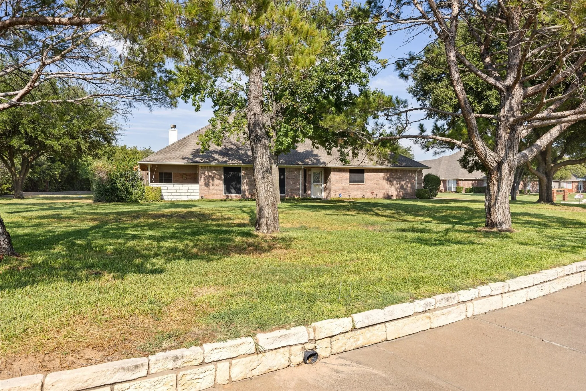 Another look at the covered entry and mature trees, and a stone retaining wall