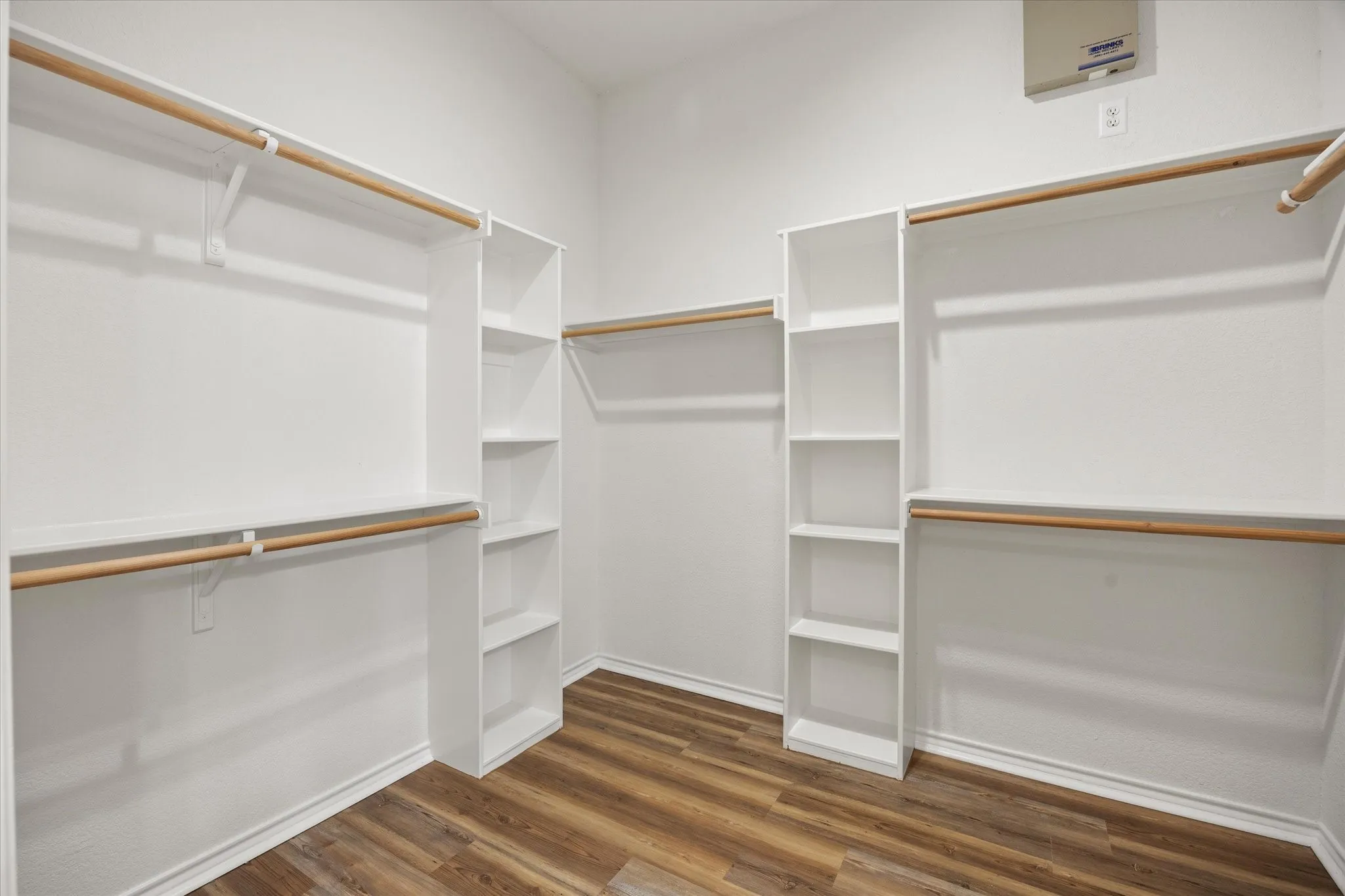 Walk-in closet with ample shelving, multiple hanging rods, and luxury vinyl plank flooring