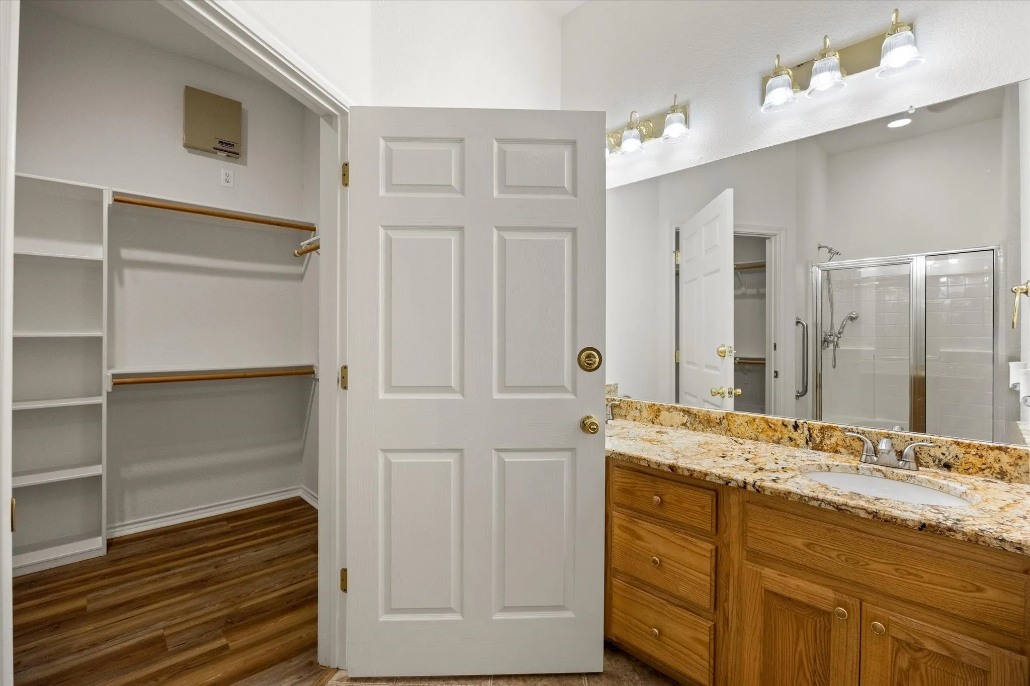 Wood-finish flooring, built-in shelving, wood vanity with a stone countertop, and glass-enclosed shower