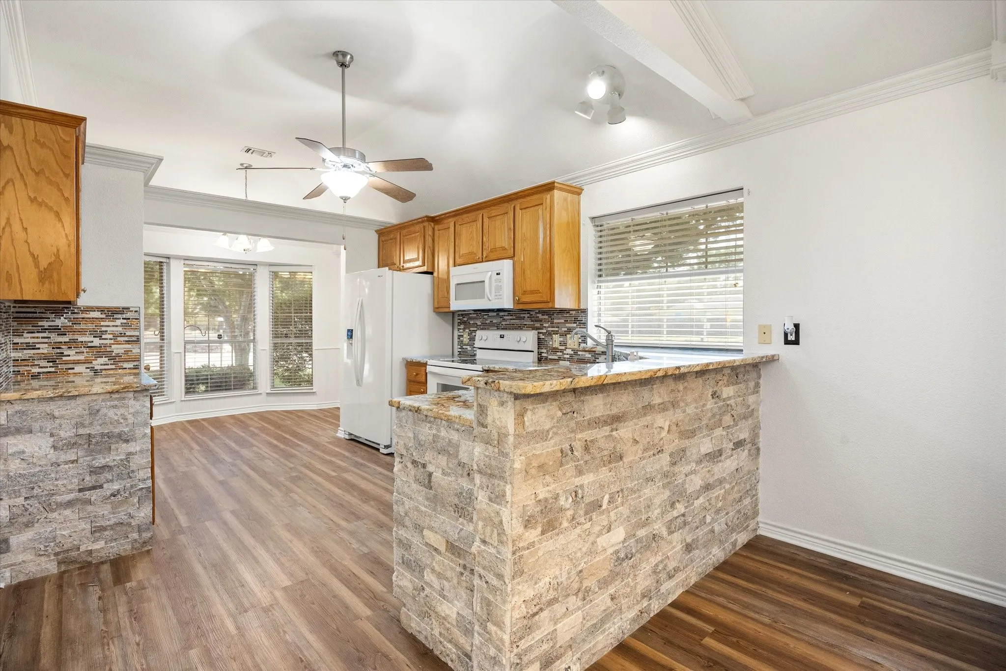 Luxury vinyl plank flooring, stone-clad breakfast bar, wood cabinetry, bay window at eating area, and crown​​‌​​​​‌​​‌‌​‌‌​​​‌‌​‌​‌​‌​​​‌​​ molding