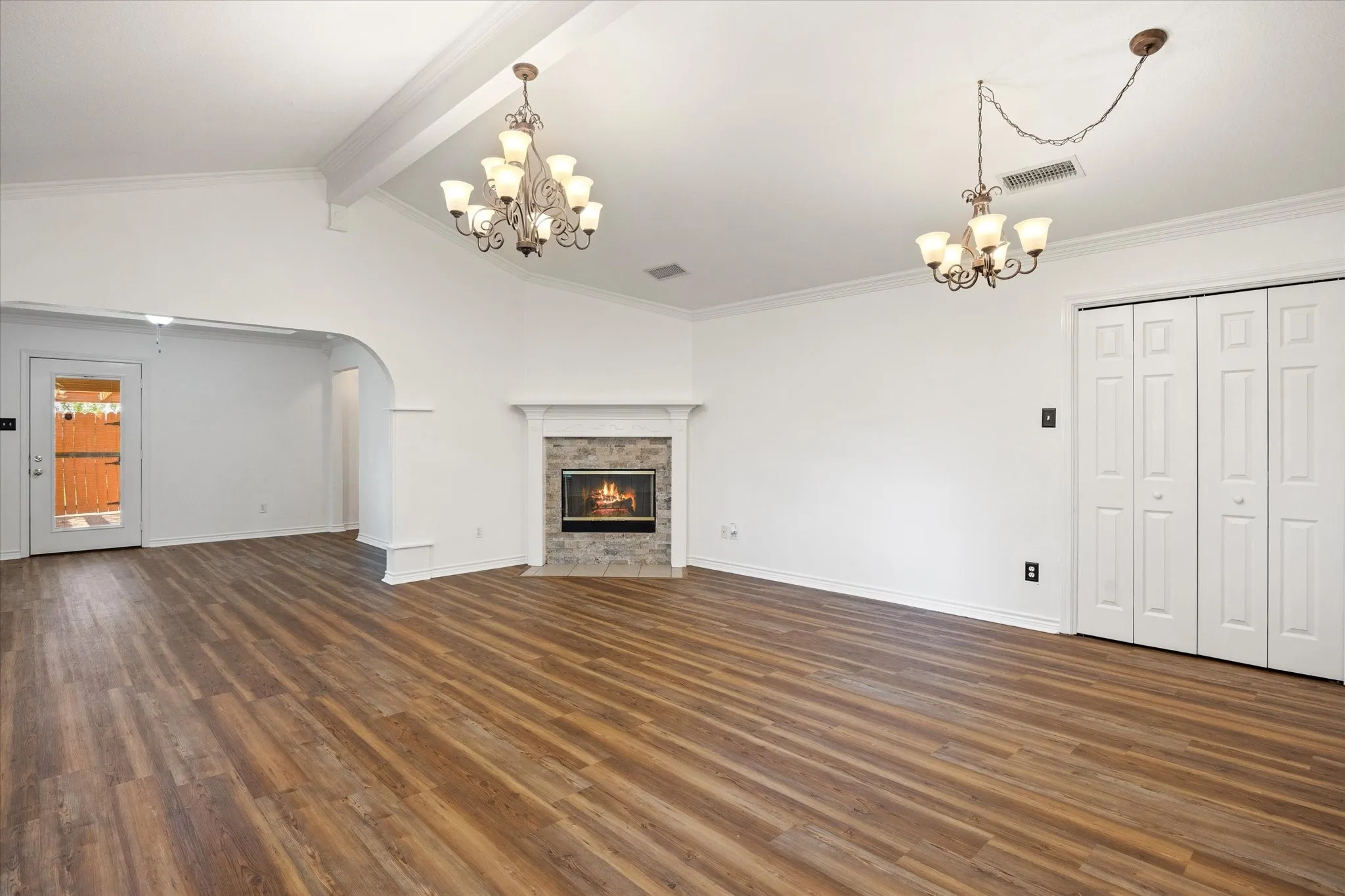 Vaulted ceiling with exposed beams, Luxury vinyl plank flooring, corner fireplace with stone surround, arched doorway, and closet