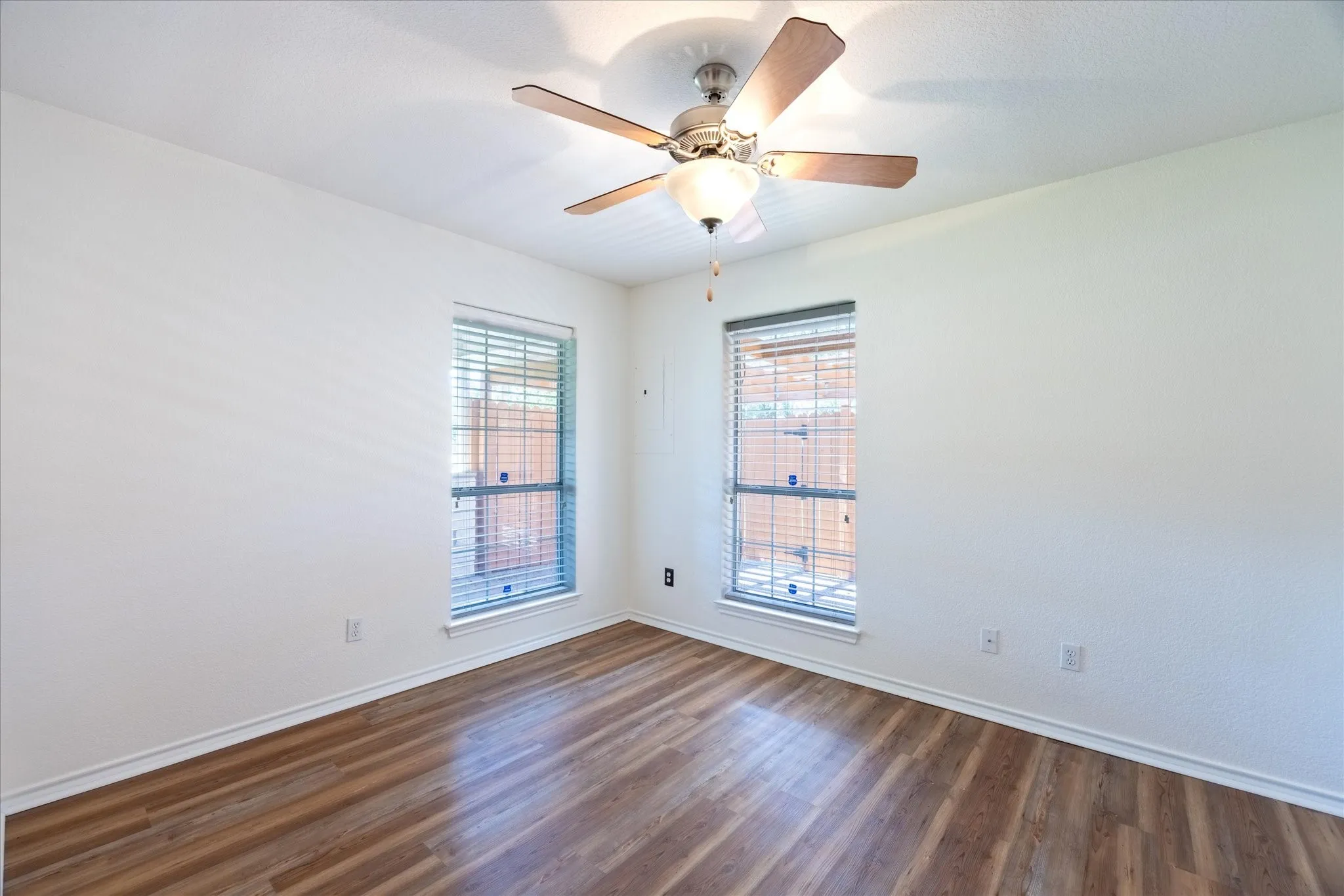 Another look at the 2nd bedroom with LVP flooring, two windows with blinds, ceiling fan with integrated lighting