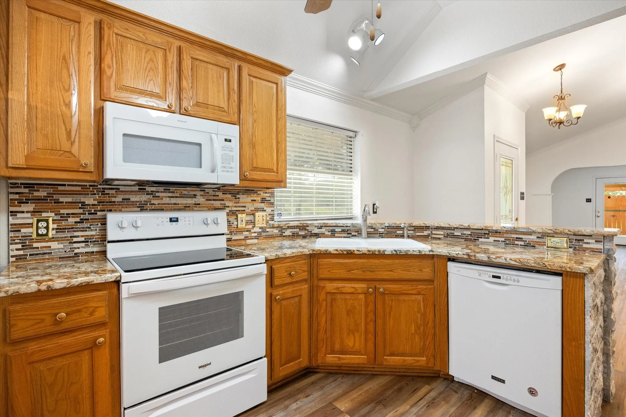 Wood-finish flooring, wood cabinetry, stone countertops, glass tile backsplash, and vaulted ceilings