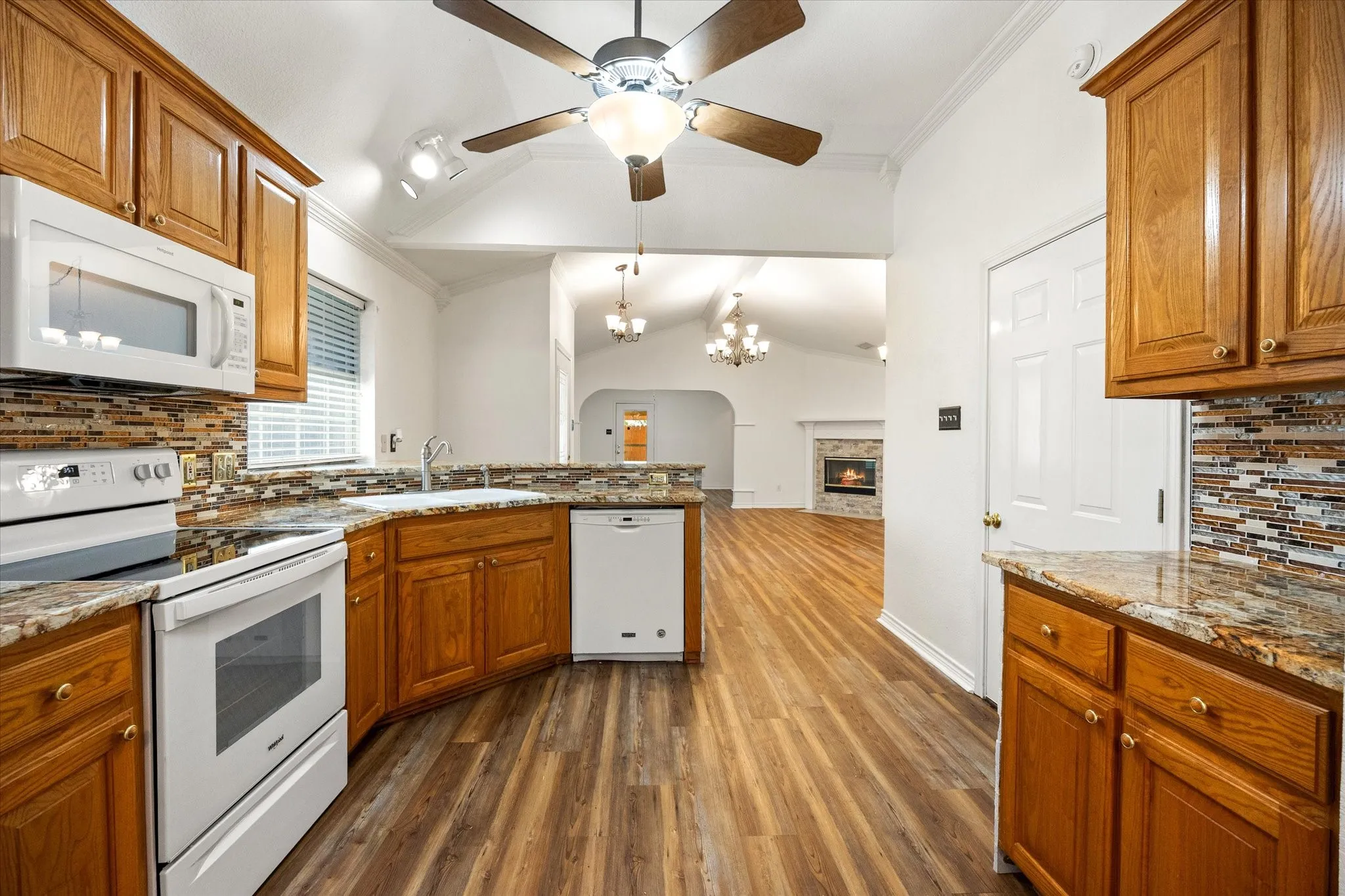 Kitchen with luxury vinyl plank flooring, wood cabinetry, granite countertops, and mosaic tile backsplash