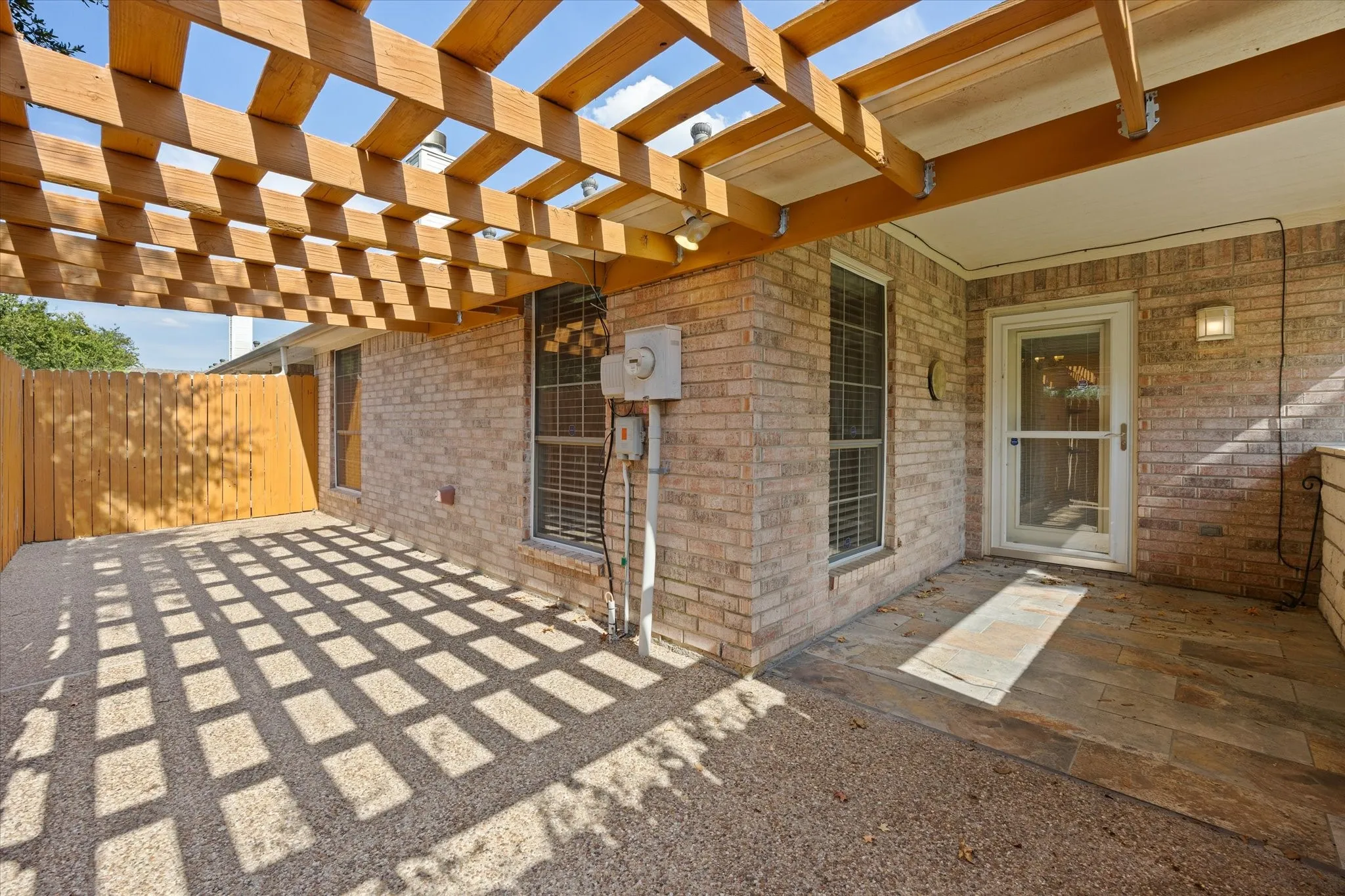 Brick exterior with a wooden pergola, privacy fence, exposed aggregate concrete patio, and slate tile