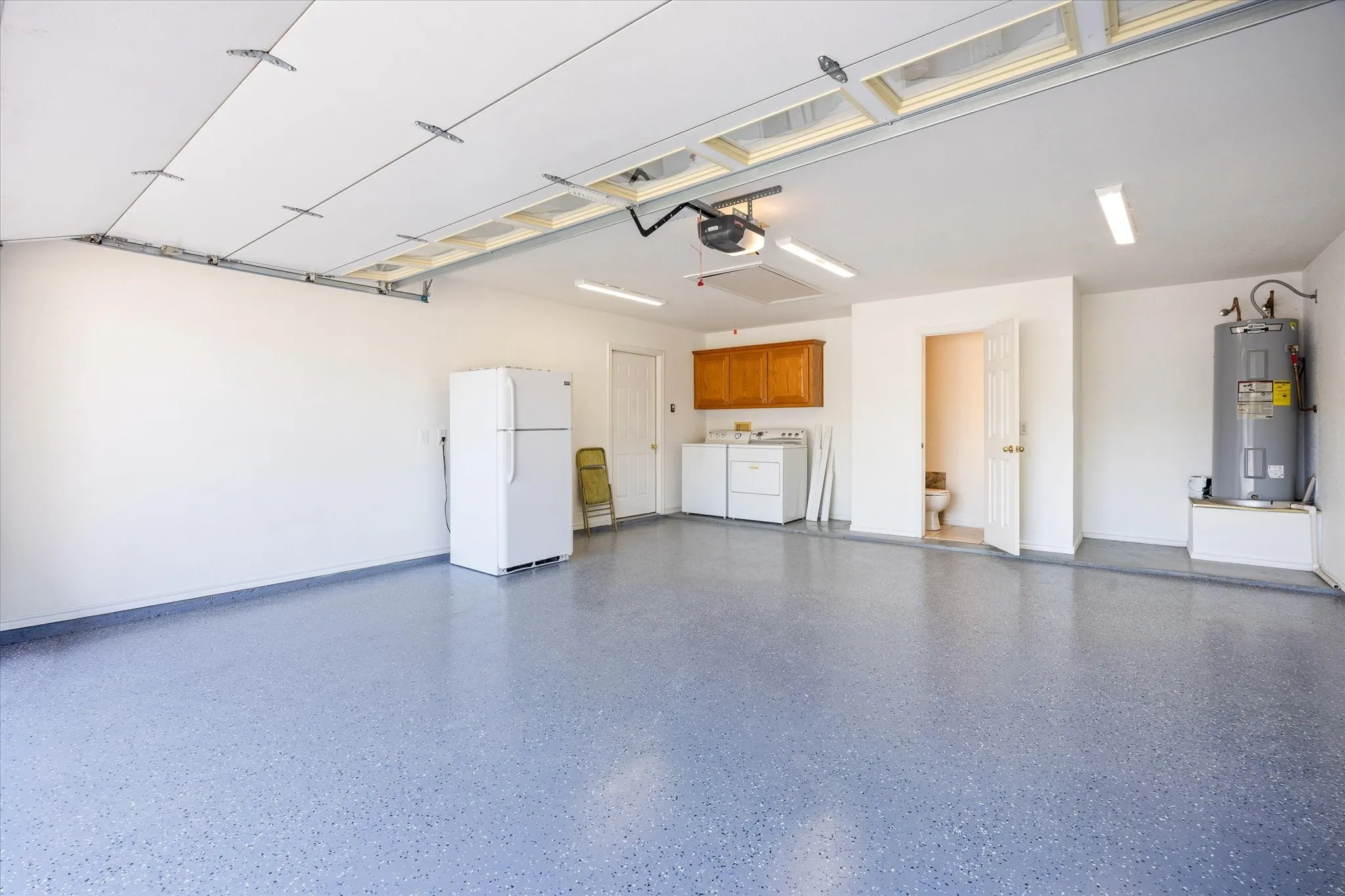 Spacious garage featuring a durable epoxy flooring finish, overhead garage door opener, and fluorescent lighting, and insulated garage door