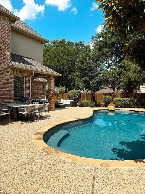 Brick exterior, covered patio, freeform swimming pool, and stone coping
