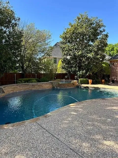Curved swimming pool with stone coping, textured aggregate decking, and a stone-clad water feature