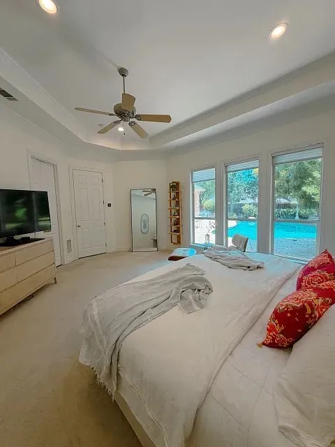 Tray ceiling with recessed lighting, ceiling fan, multiple windows, and light-toned carpeting