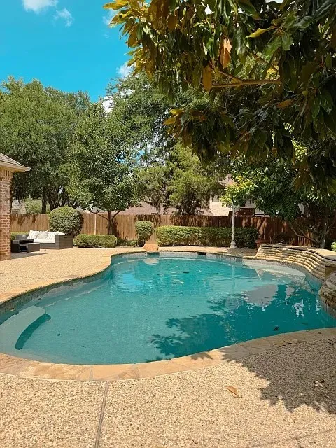 Freeform swimming pool with a stone coping and aggregate concrete decking, complemented by mature trees and landscaping