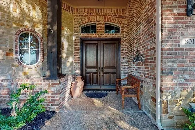 Brick and stone exterior with a prominent wooden double door entry, featuring an arched transom window