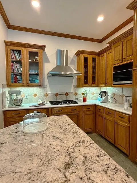 Kitchen featuring granite countertops, wood cabinetry, stainless steel range hood, built-in microwave, and tile backsplash