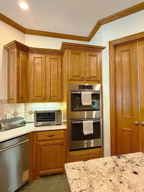 Wood-finish cabinetry, stainless steel double wall ovens, recessed lighting, and a patterned tile backsplash