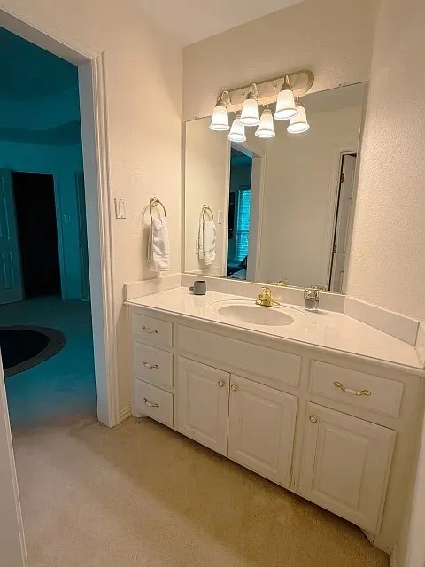 White vanity with gold-finish hardware, integrated sink, and wall-mounted light fixture