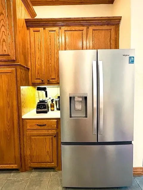 Stainless steel French door refrigerator with bottom freezer, wood-finish cabinetry, under-cabinet lighting, and light-toned countertop