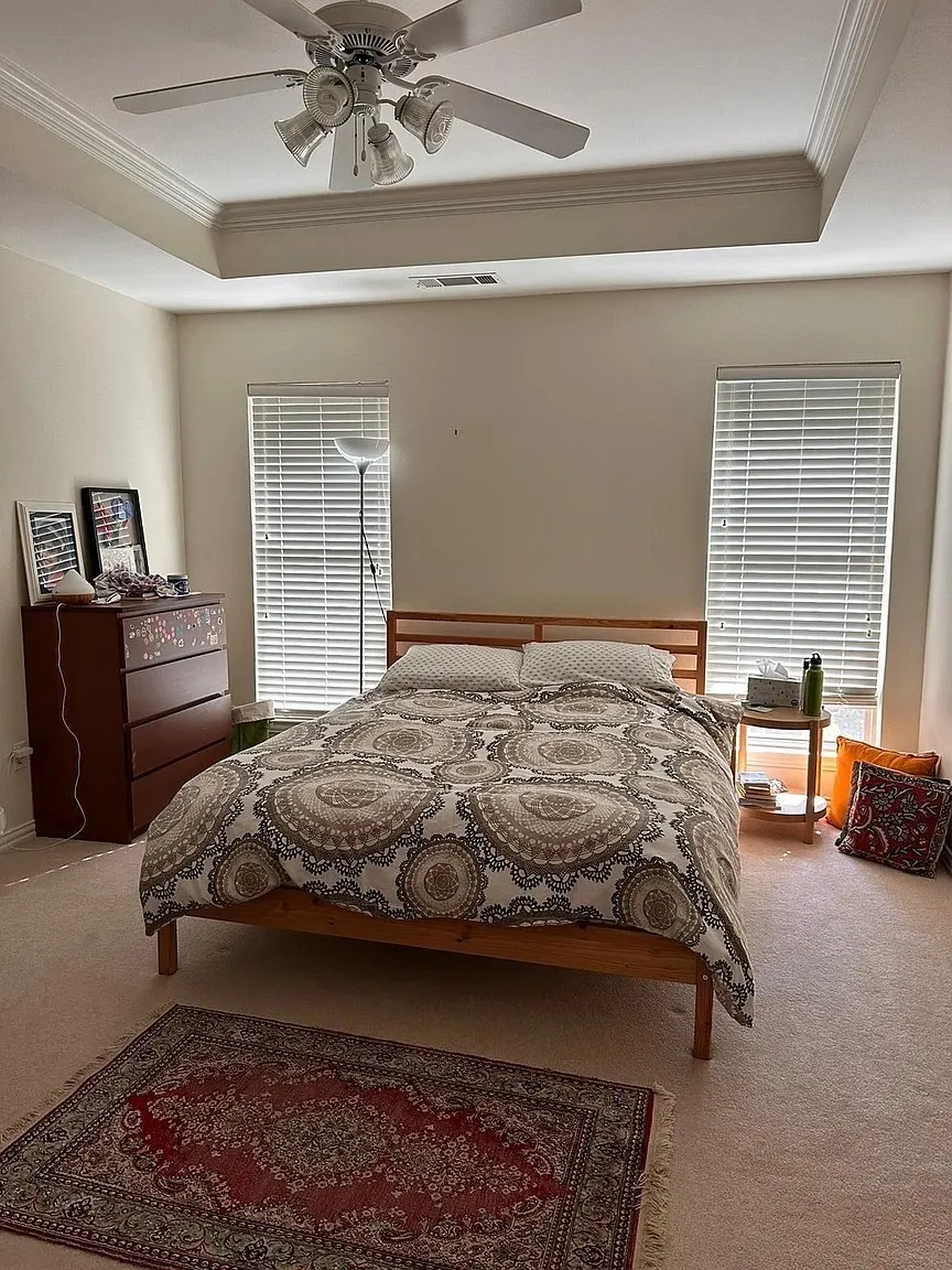 Tray ceiling with crown molding, ceiling fan with integrated lighting, two windows with horizontal blinds, and neutral carpet flooring