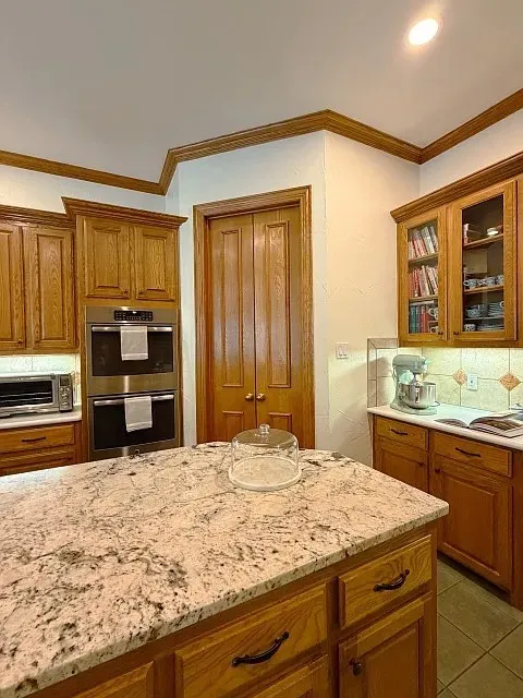 Kitchen island with a light-toned countertop, wood cabinetry, double wall ovens, and tile flooring