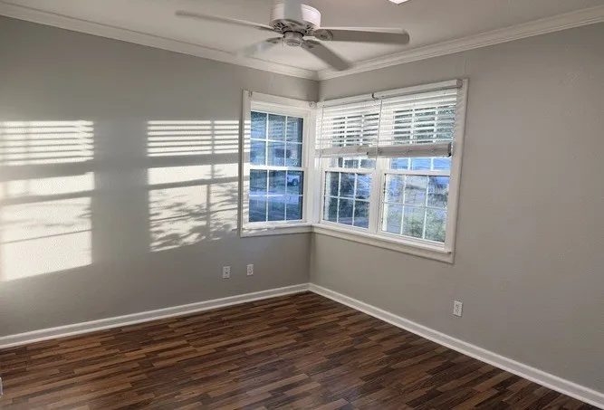 Wood-finish flooring, white window blinds, white trim, and a ceiling fan with integrated lighting