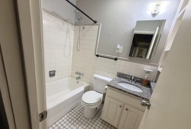 Bathroom featuring a white bathtub, ceramic wall tiling, hexagon tile flooring, and a vanity with a stone countertop