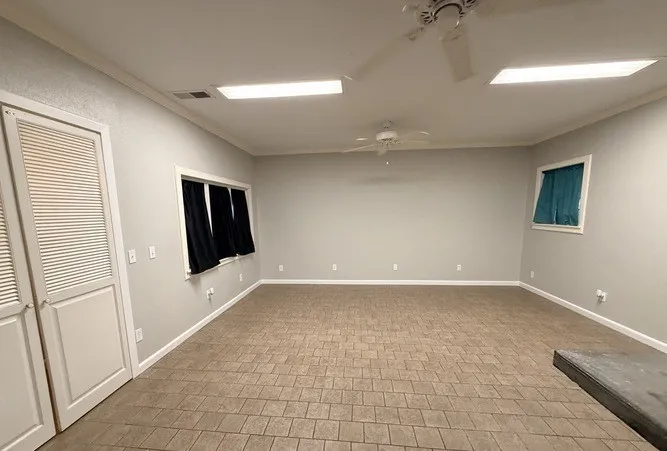 Spacious room featuring tile flooring, neutral wall tones, crown molding, and dual ceiling fans
