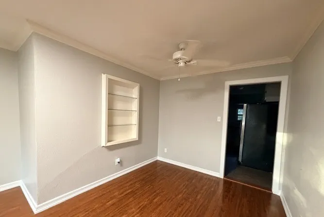 Wood-finish flooring, built-in display shelving, crown molding, ceiling fan, and painted walls