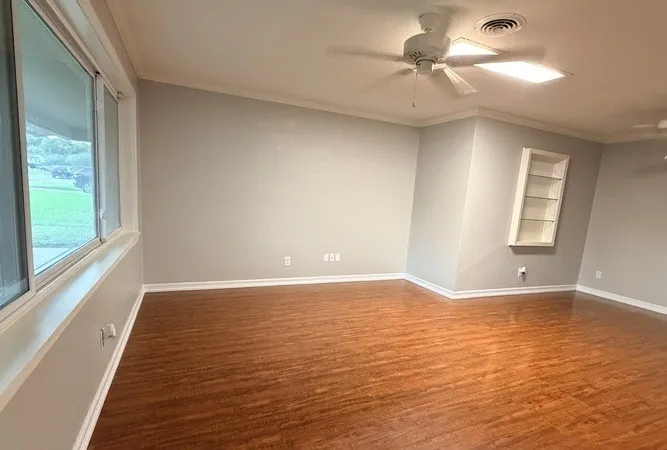 Wood-finish flooring, built-in shelving, crown molding, ceiling fan, and large windows