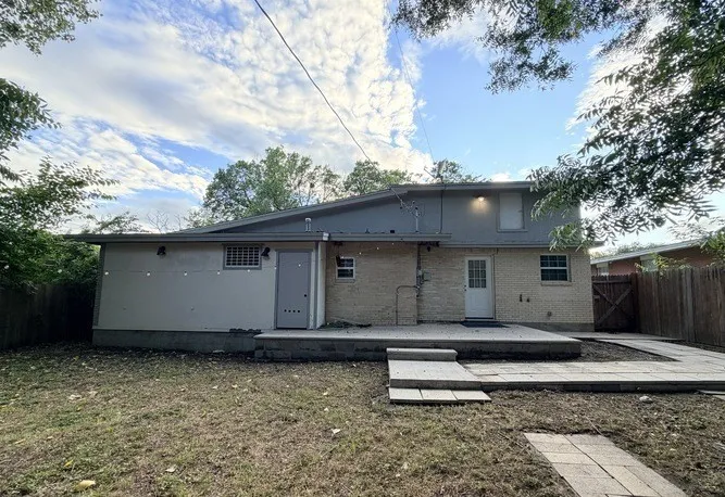 Rear exterior featuring a brick facade, integrated patio space, upper-level accent lighting, and a partial privacy fence