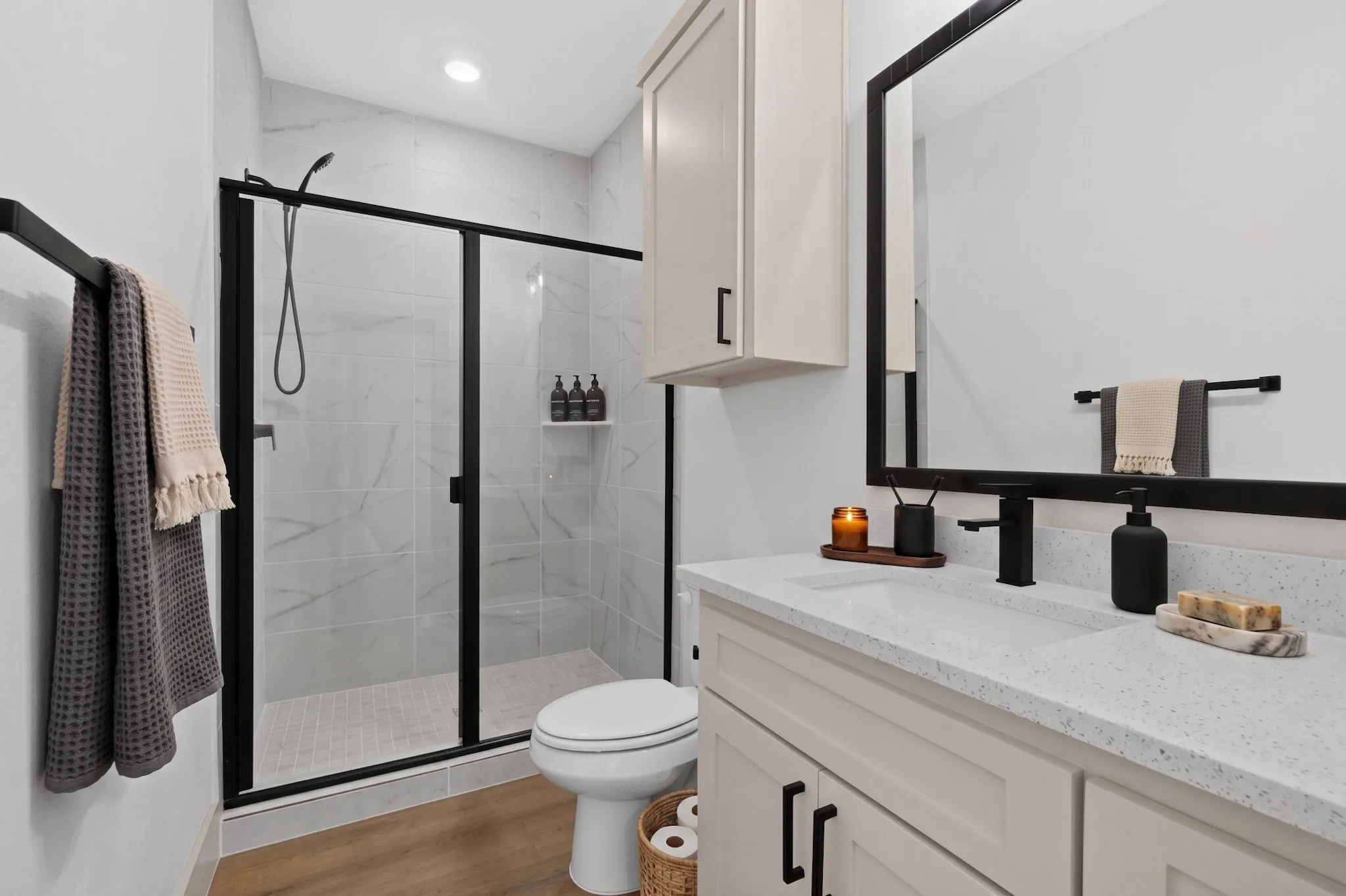 (Virtual Staging)Modern primary bathroom featuring a frameless glass-enclosed shower with subway tile surround, dual vanity with quartz countertop, matte black hardware and fixtures, recessed lighting, and wood-finish flooring
