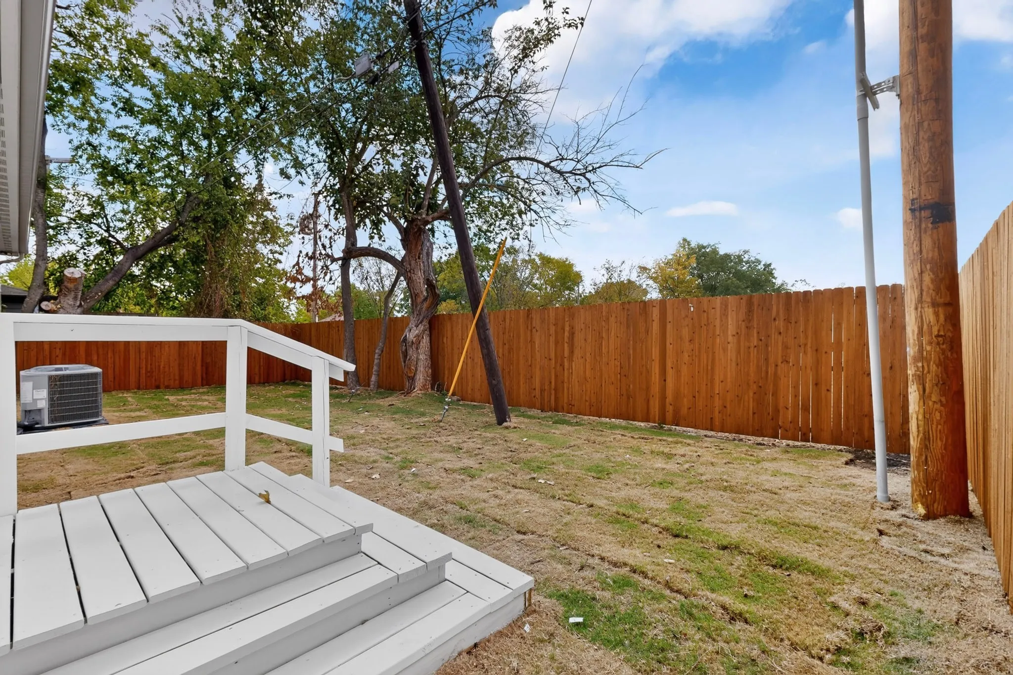 Expansive backyard featuring a wood fence, mature trees, and a white deck with steps