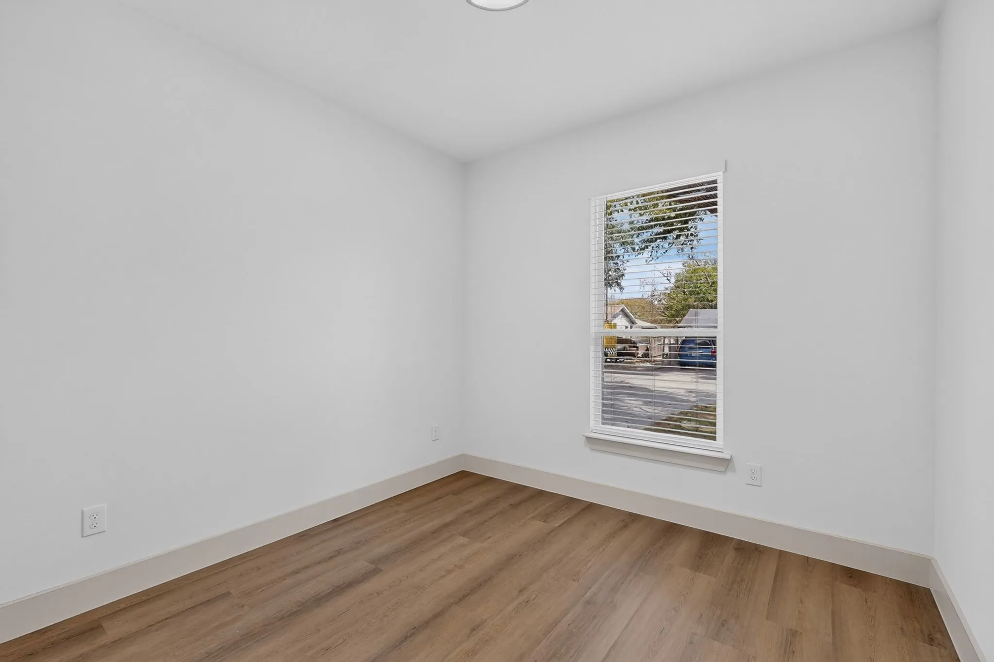 Wood-finish flooring, white painted walls, and a single window with horizontal blinds