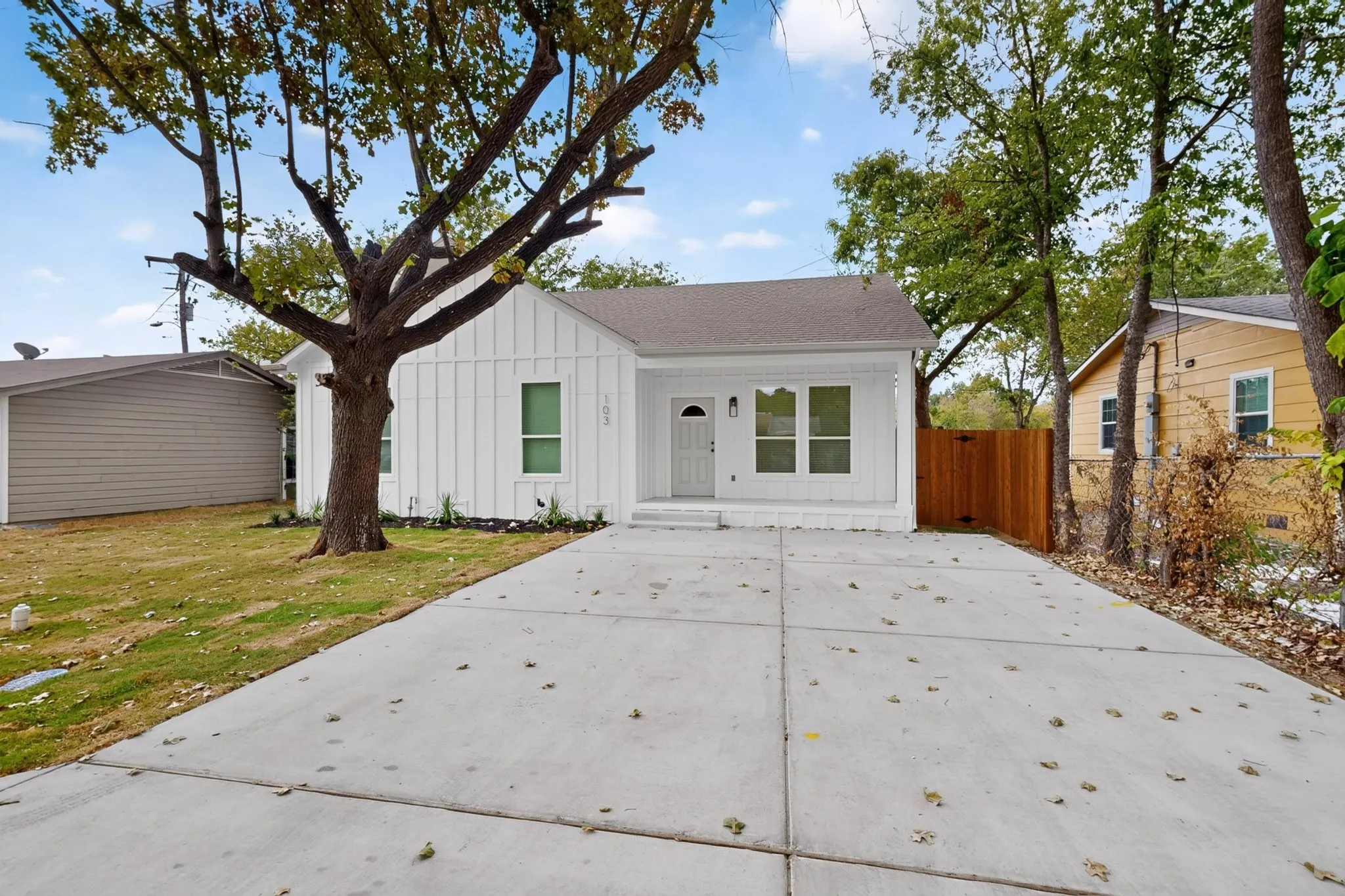 White vertical siding exterior, gabled roof, concrete driveway, front entrance, and a wood fence