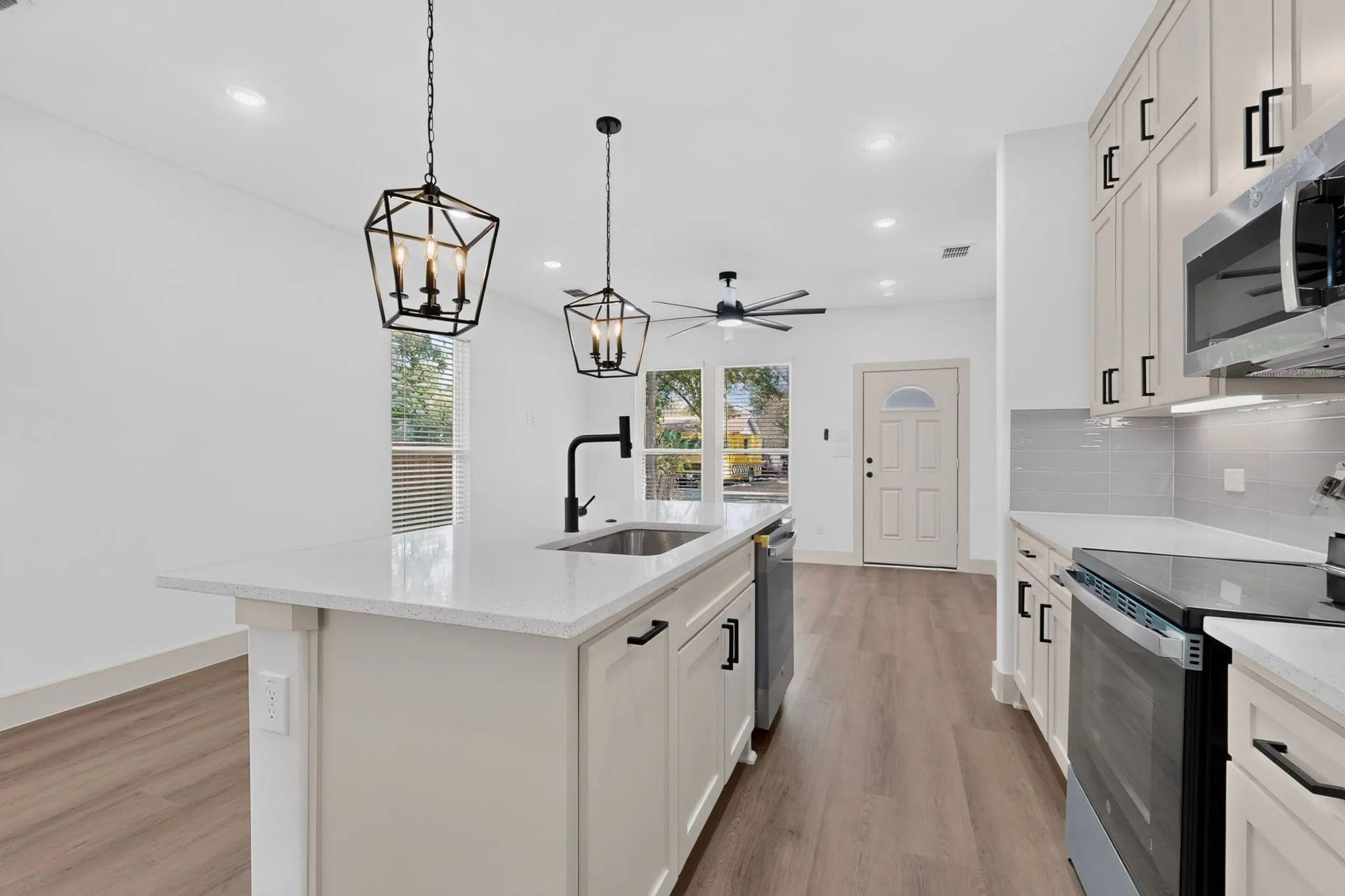 Open-concept kitchen with white shaker cabinetry, light-toned countertops, a matte black faucet, and wood-finish flooring