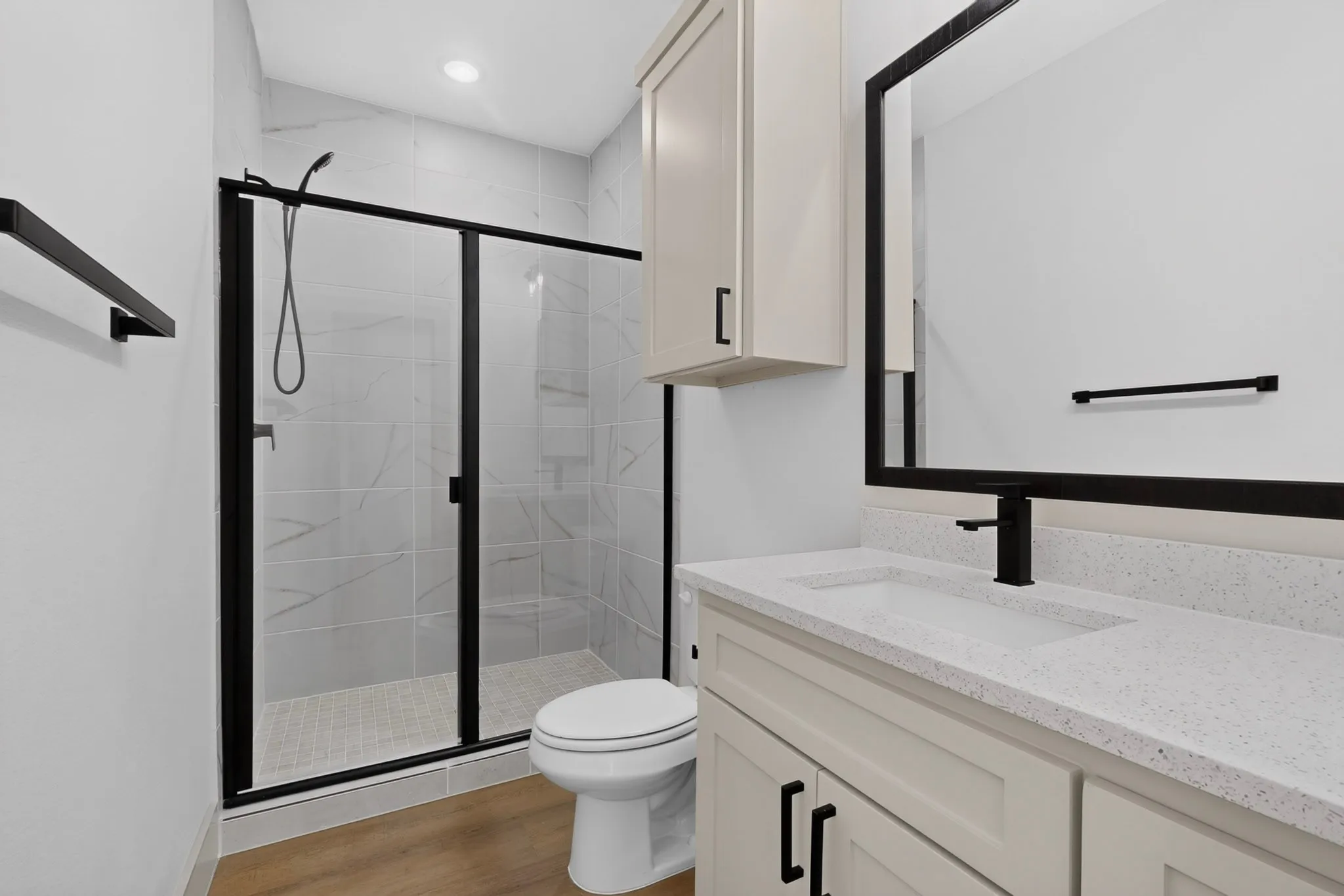 Walk-in shower with clear glass enclosure and black frame, white tiled shower walls, built-in vanity with light-toned cabinetry, white countertop, and black fixtures